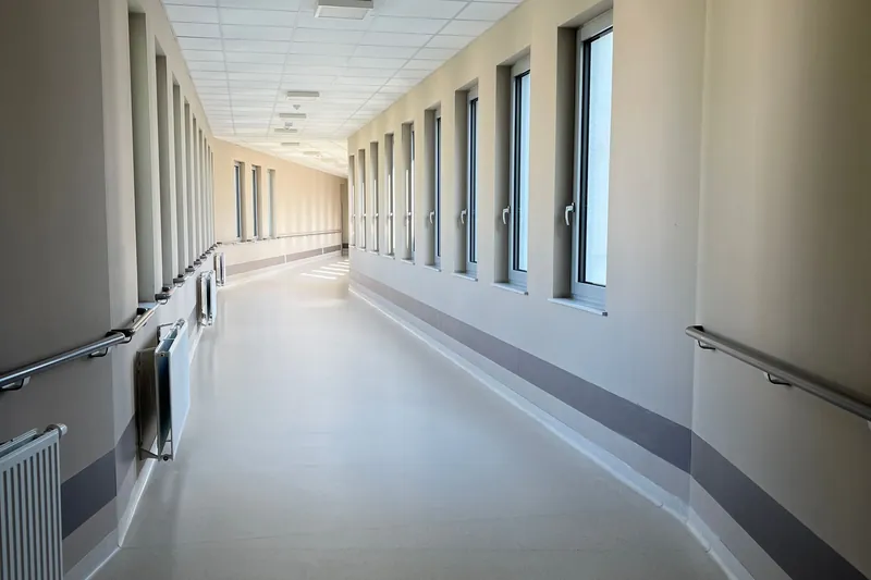 Bright empty hospital corridor with tall windows and handrails