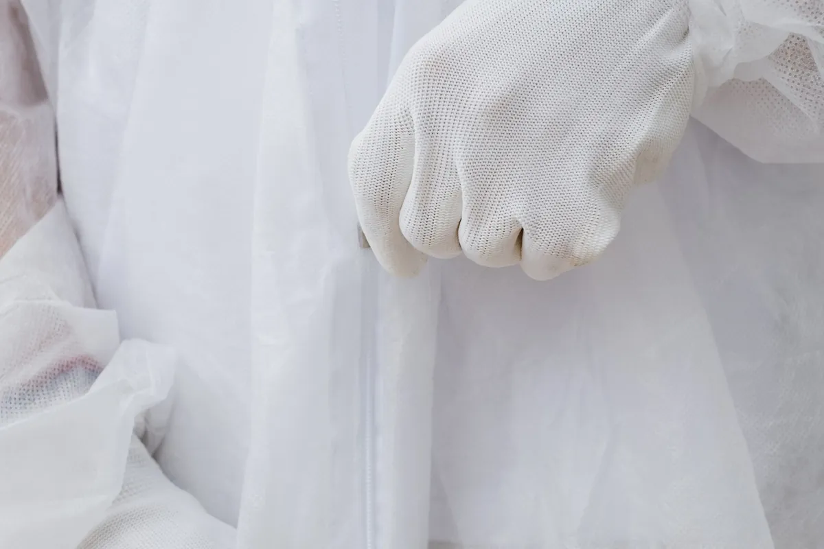 Gloved hands folded in front of a white disposable protective suit